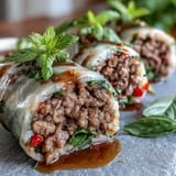 Delicious Thai Basil Beef Rolls plated with fresh cucumbers, carrots, and herbs, showcasing the tender beef and rice paper texture.