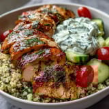 A vibrant Greek Chicken Power Bowl with grilled lemon-herb chicken breast over fluffy quinoa, topped with fresh cucumbers, cherry tomatoes, and a dollop of creamy tzatziki sauce.