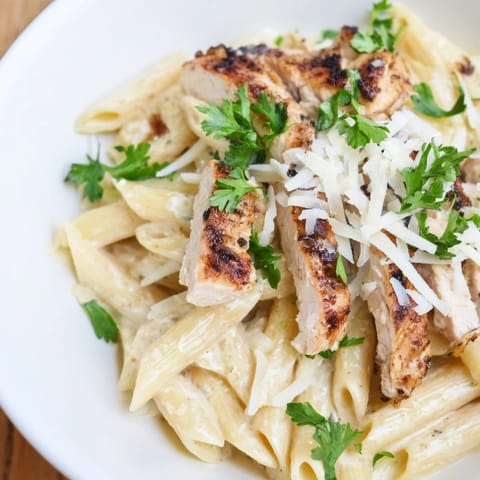 A hearty bowl of Spicy Chicken Caesar Pasta topped with parmesan, croutons, and lemon wedges for bright flavor.  