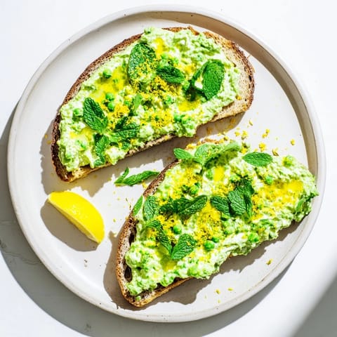 The Pea & Mint Ricotta Toast showcases a fluffy ricotta spread with bright lemon zest, served on a rustic wooden board for a fresh, light meal.