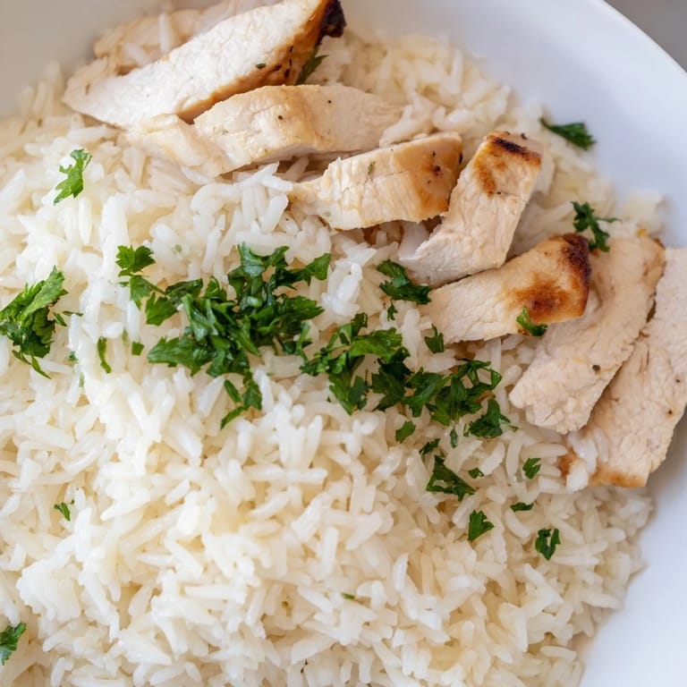 Sizzling chicken sizzles on a grill, ready to top the rich, buttery rice infused with minced garlic and herbs.