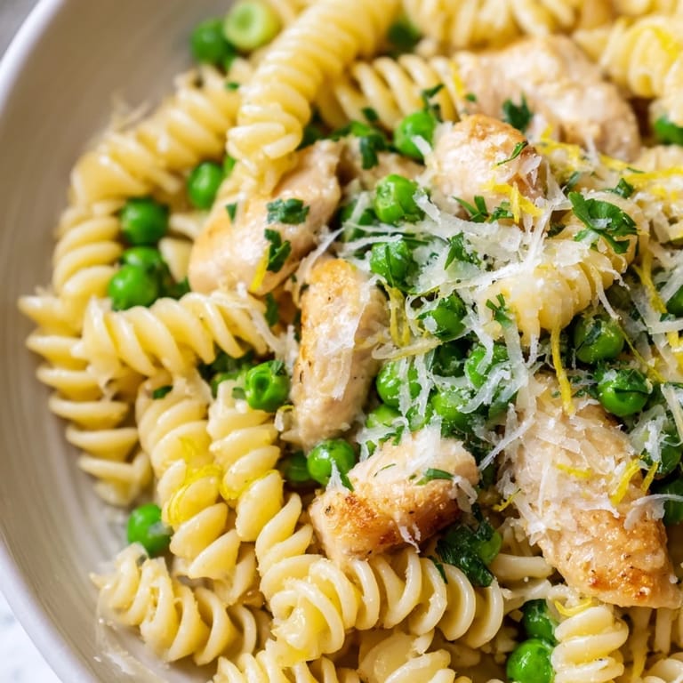 Tender rotini pasta with juicy chicken and green peas in a glossy garlic butter sauce, served warm and ready to eat.