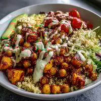 Close-up of a vibrant Buddha Bowl with Quinoa, Roasted Sweet Potatoes, and Crispy Chickpeas, topped with creamy garlic tahini dressing.